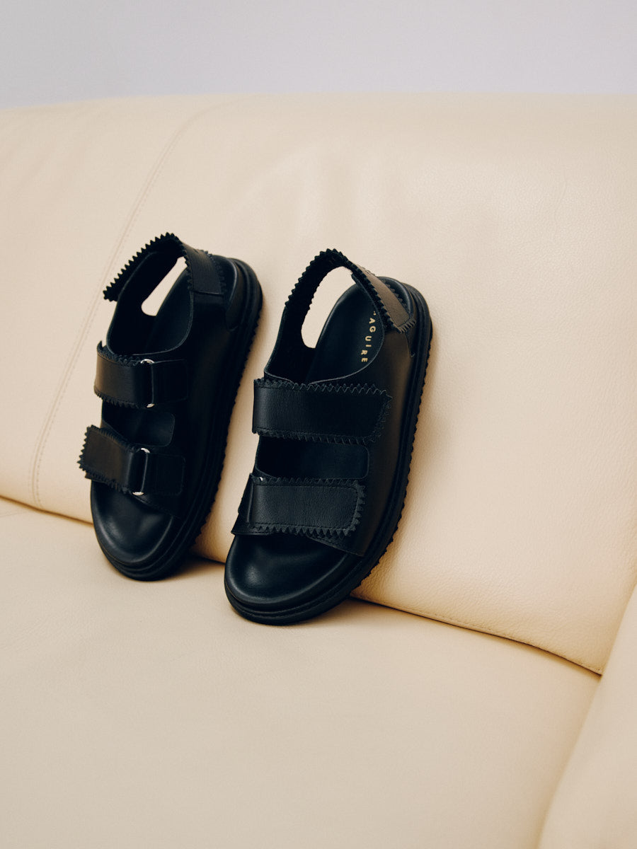 Maguire Tavira velcro straps black sandal in leather handmade in Portugal disposed on a beige couch